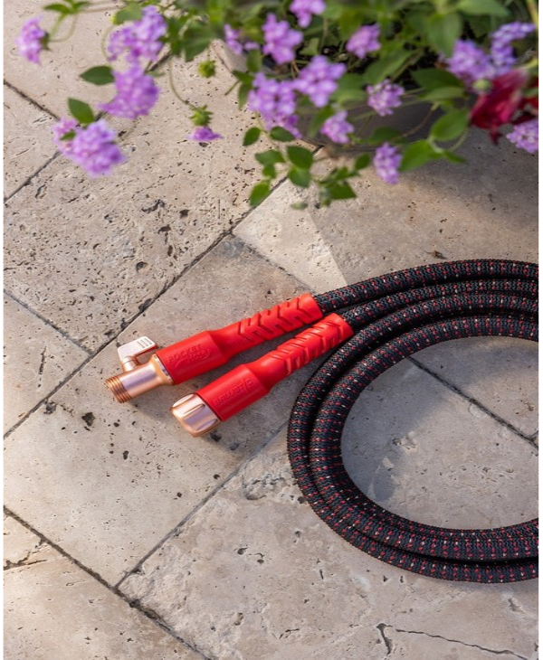 Red and black garden hose on a concrete surface with purple flowers in the background